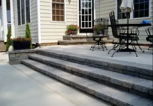Covered porch of a building with a concrete floor. Columns have stone bases. Asphalt parking lot visible.