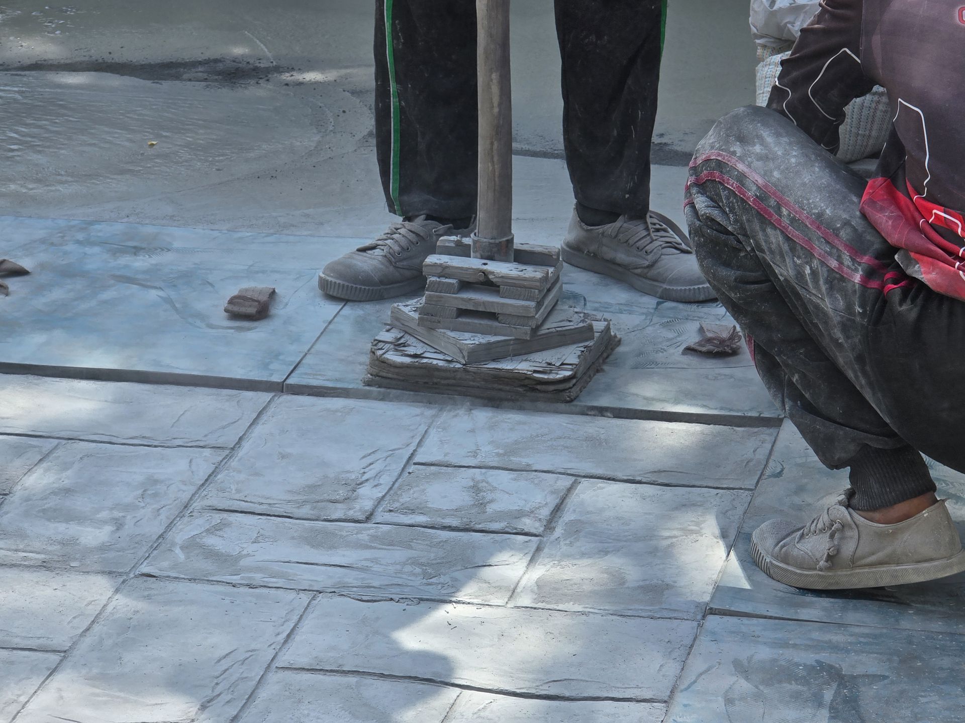 Workers stamping concrete pavement with a metal tool outdoors.