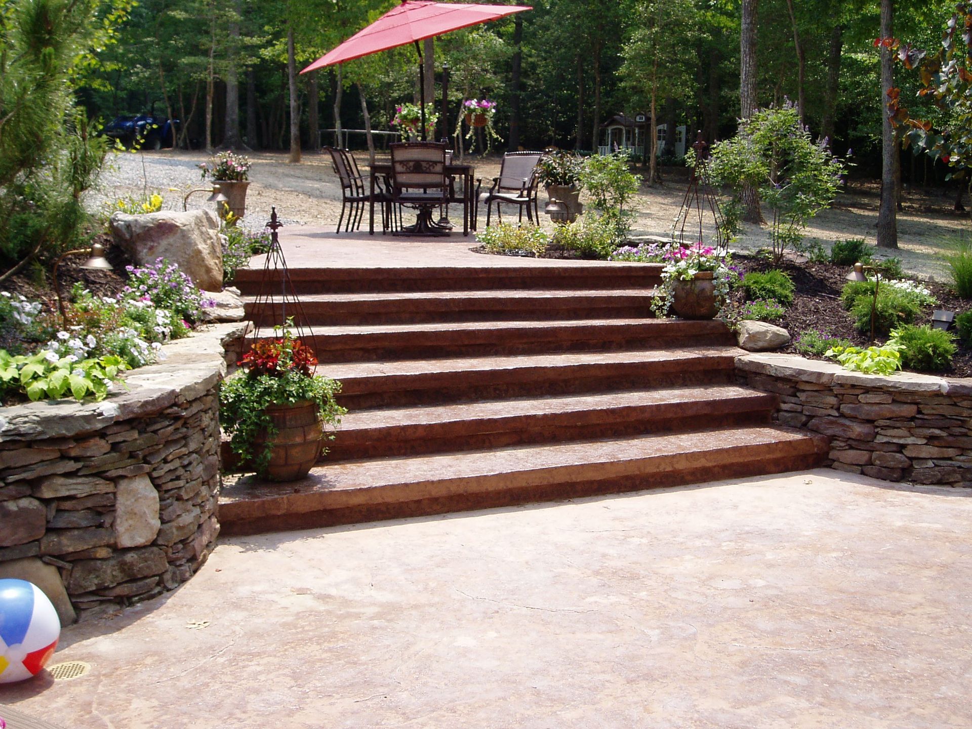 Stone steps lead up to a patio with a table and umbrella. Flower pots line the steps.