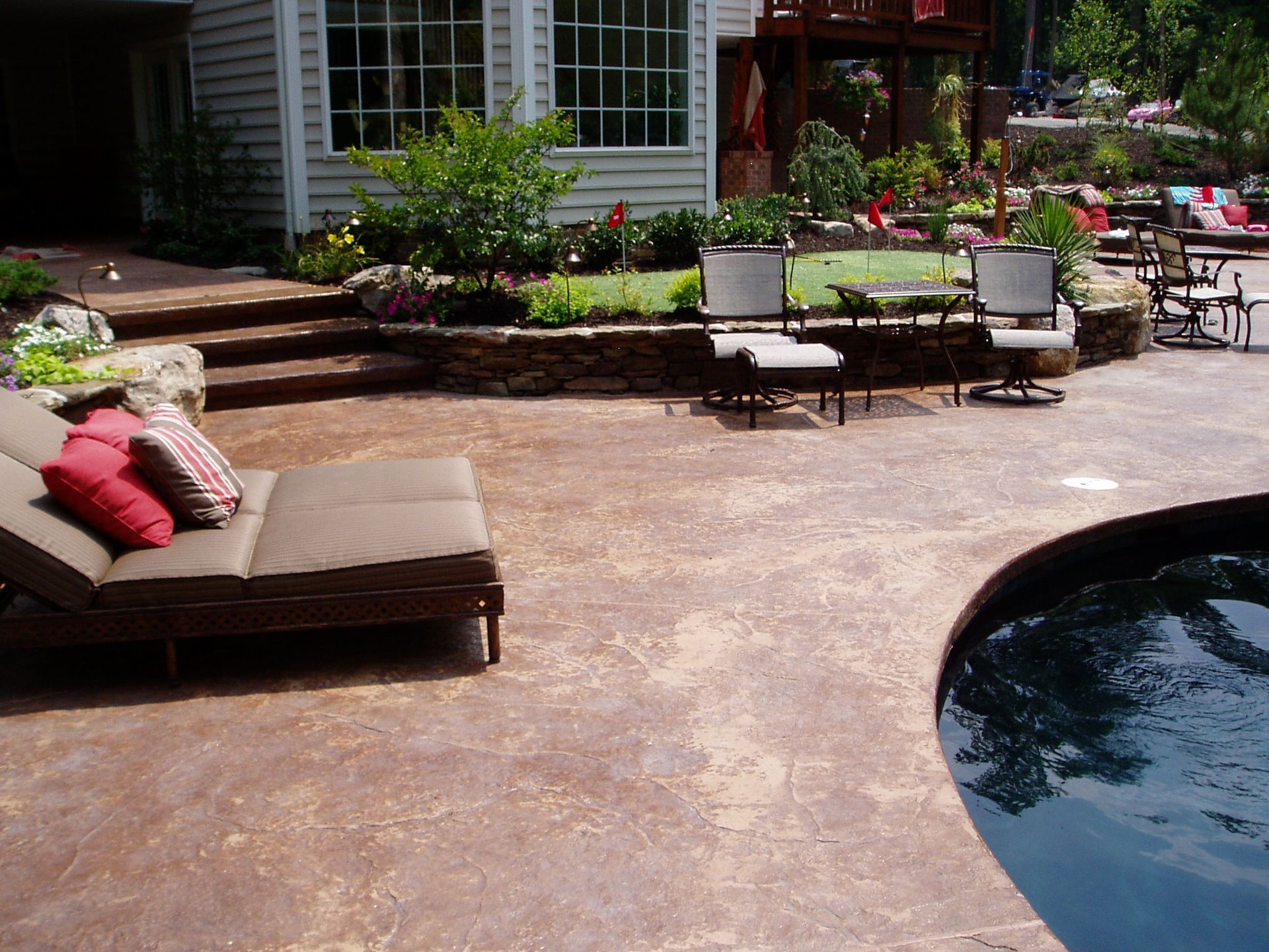 Patio with lounge chair, pool, seating area, and landscaping near a house.