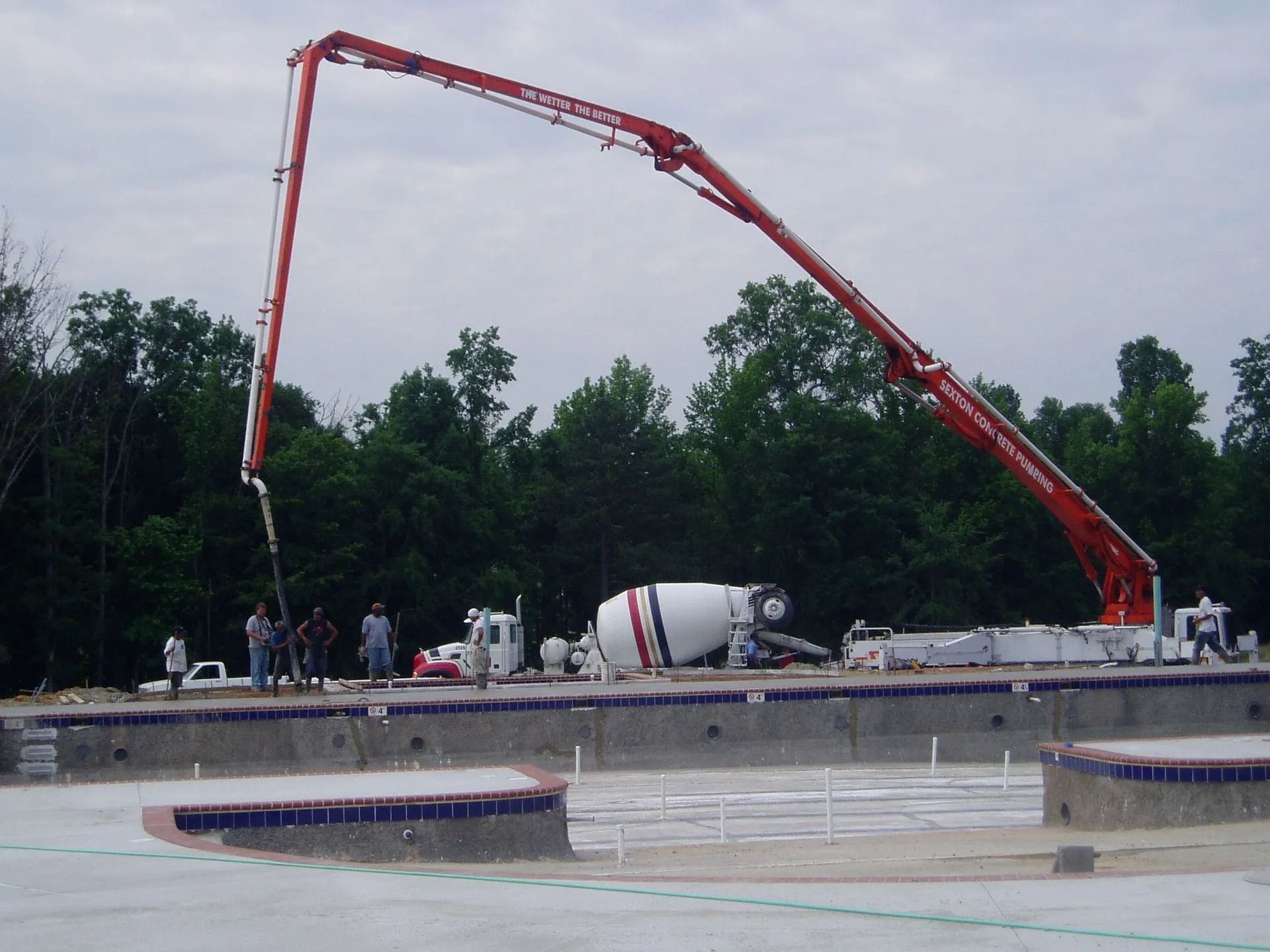 Red concrete pump pouring at a highway construction site with workers and a cement mixer truck.
