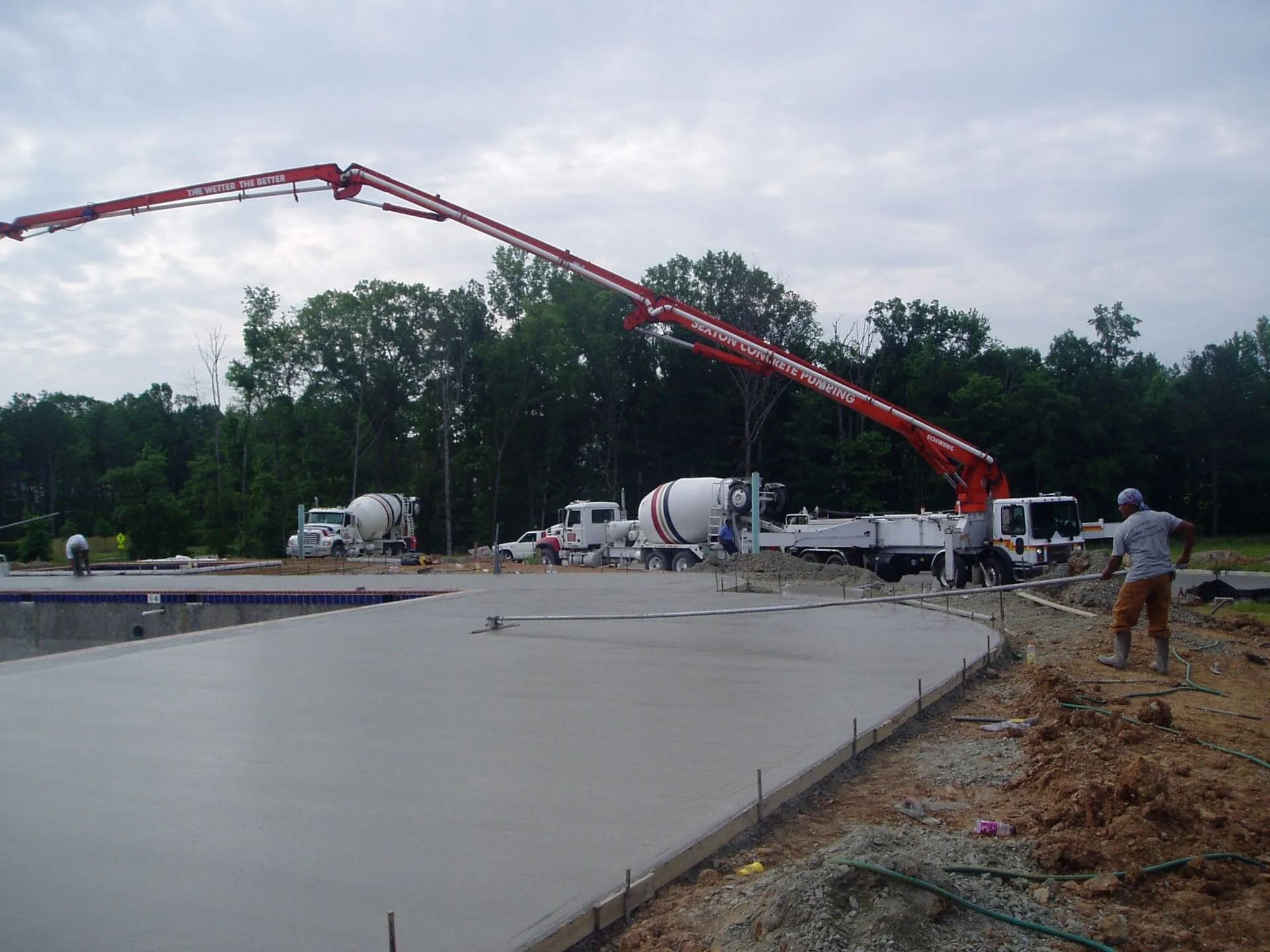 Concrete being poured on a large roadway construction site with a long red boom pump and workers nearby