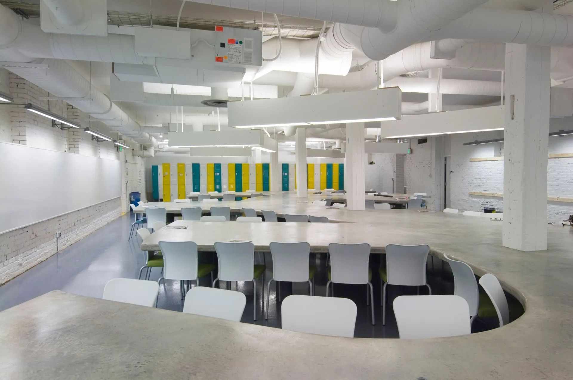 Modern white cafeteria with rows of tables, chairs, and colorful lockers in the background