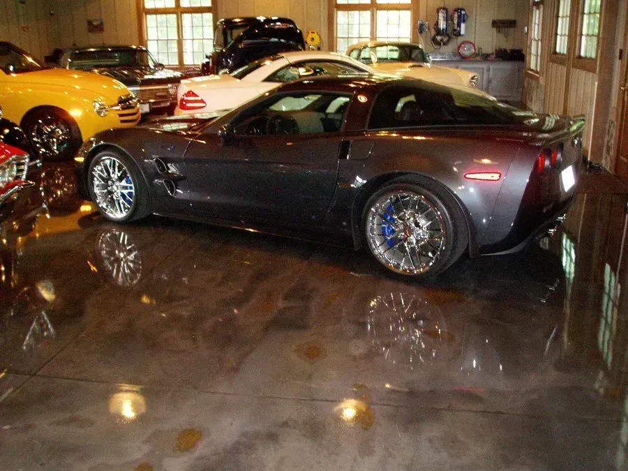 Gray Corvette parked in a garage with a glossy, reflective floor, surrounded by other vehicles.