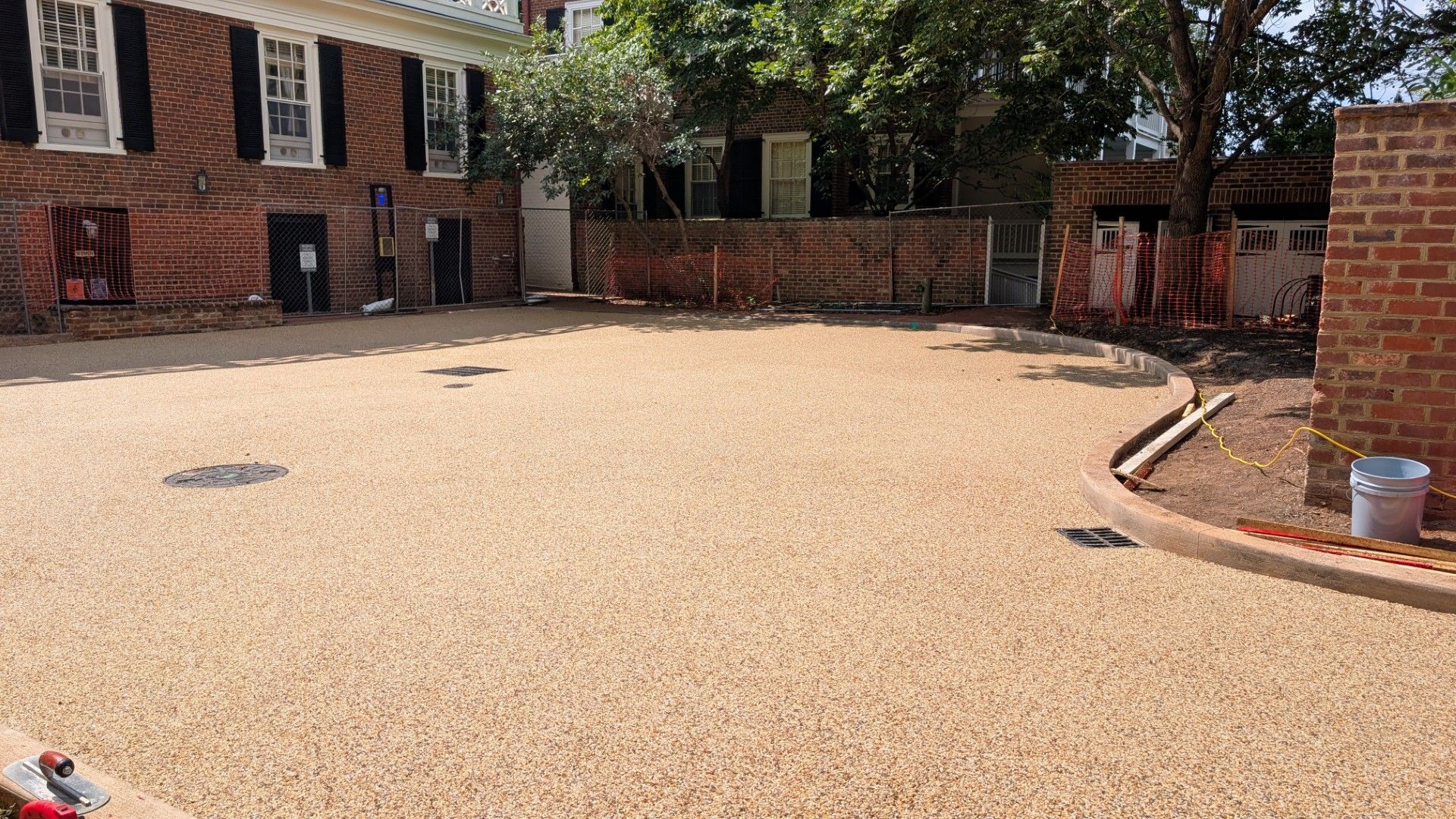 Empty gravel courtyard beside brick townhouses with a wood fence and a bucket near the right wall.