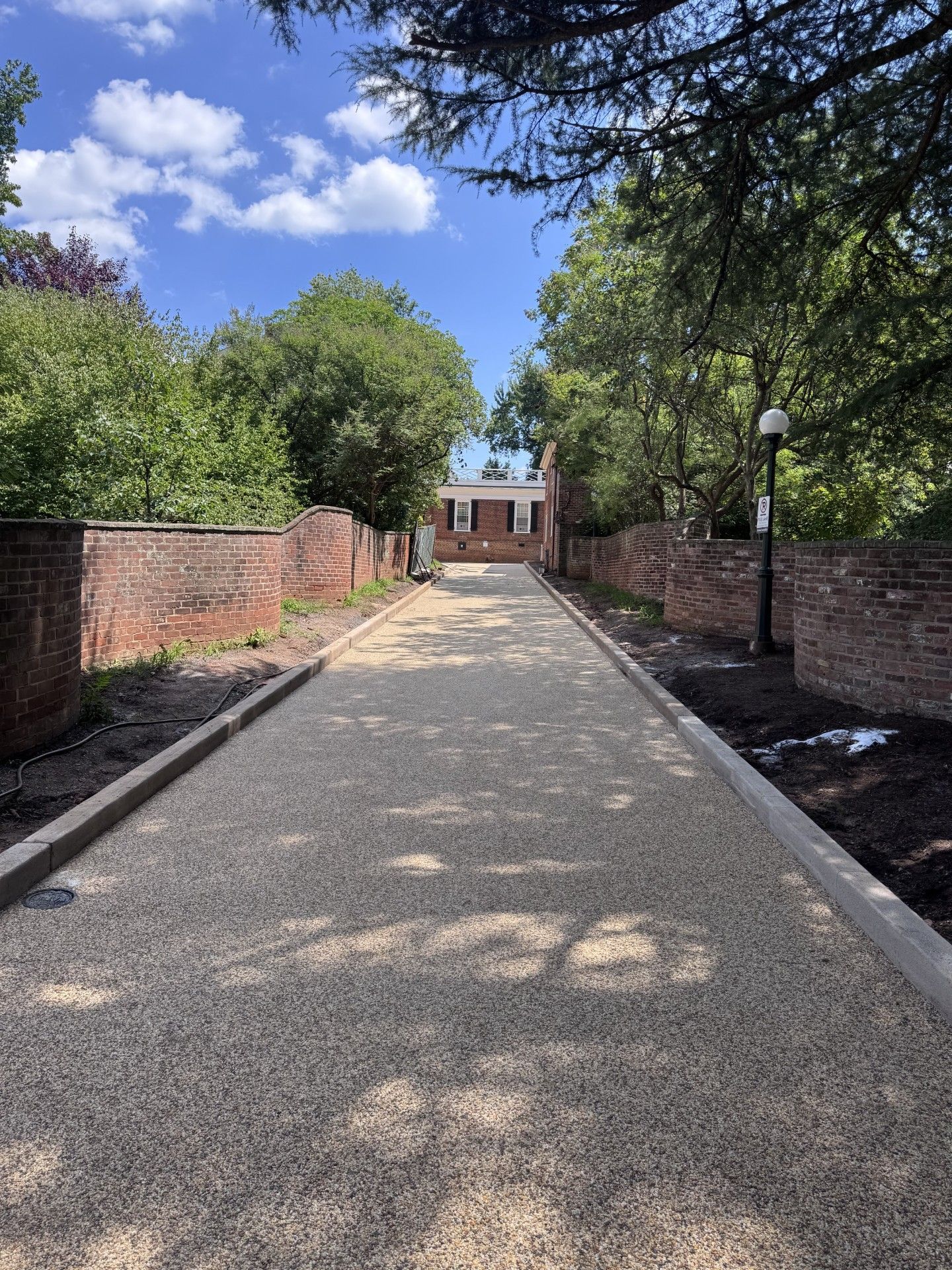 Brick walkway lined with trees and lampposts leading to a building under a blue sky