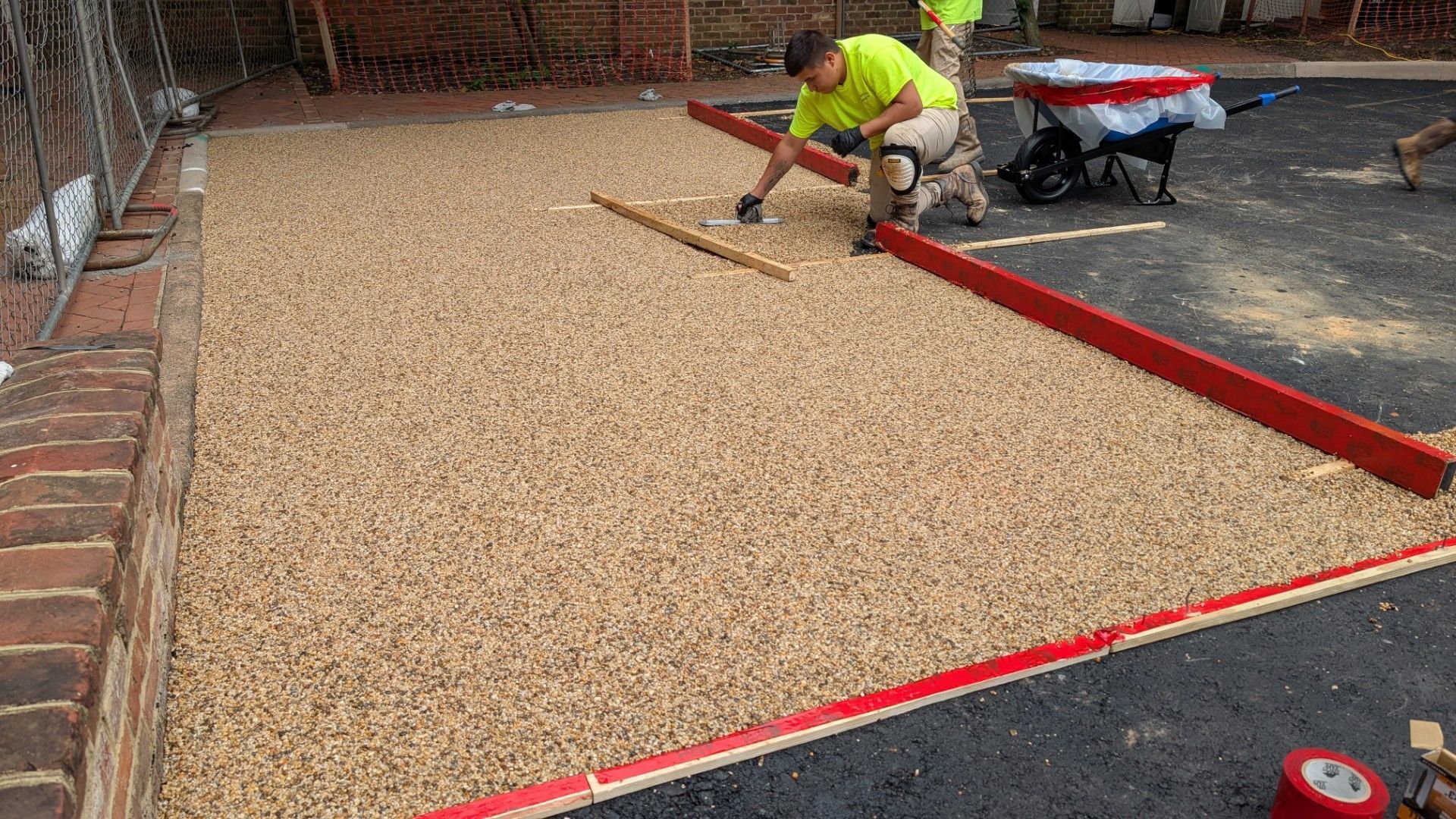 Worker installing a tan gravel surface with red edging in a driveway area