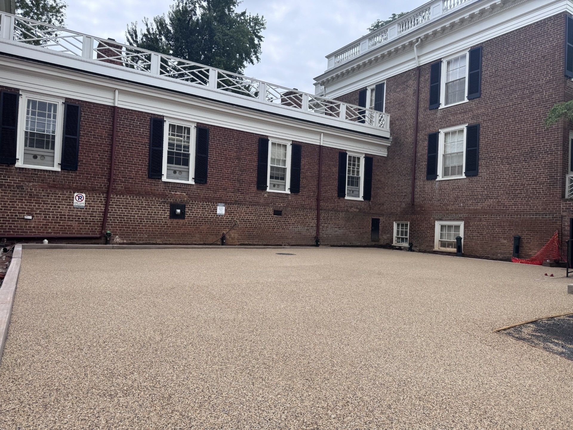 Brick building with white trim and windows behind a large gravel courtyard
