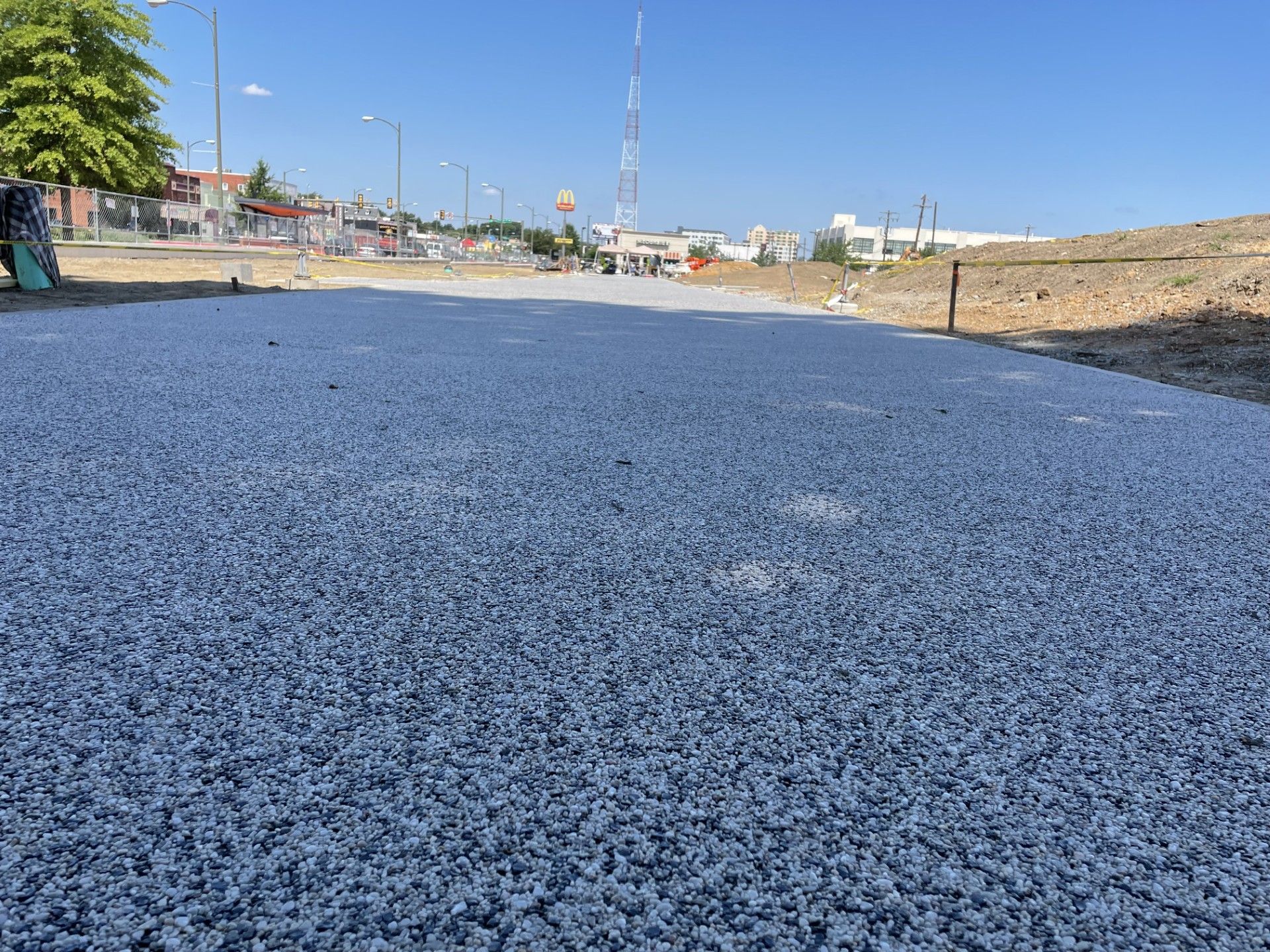 Freshly paved blue road beside a sidewalk with streetlights and buildings in the distance