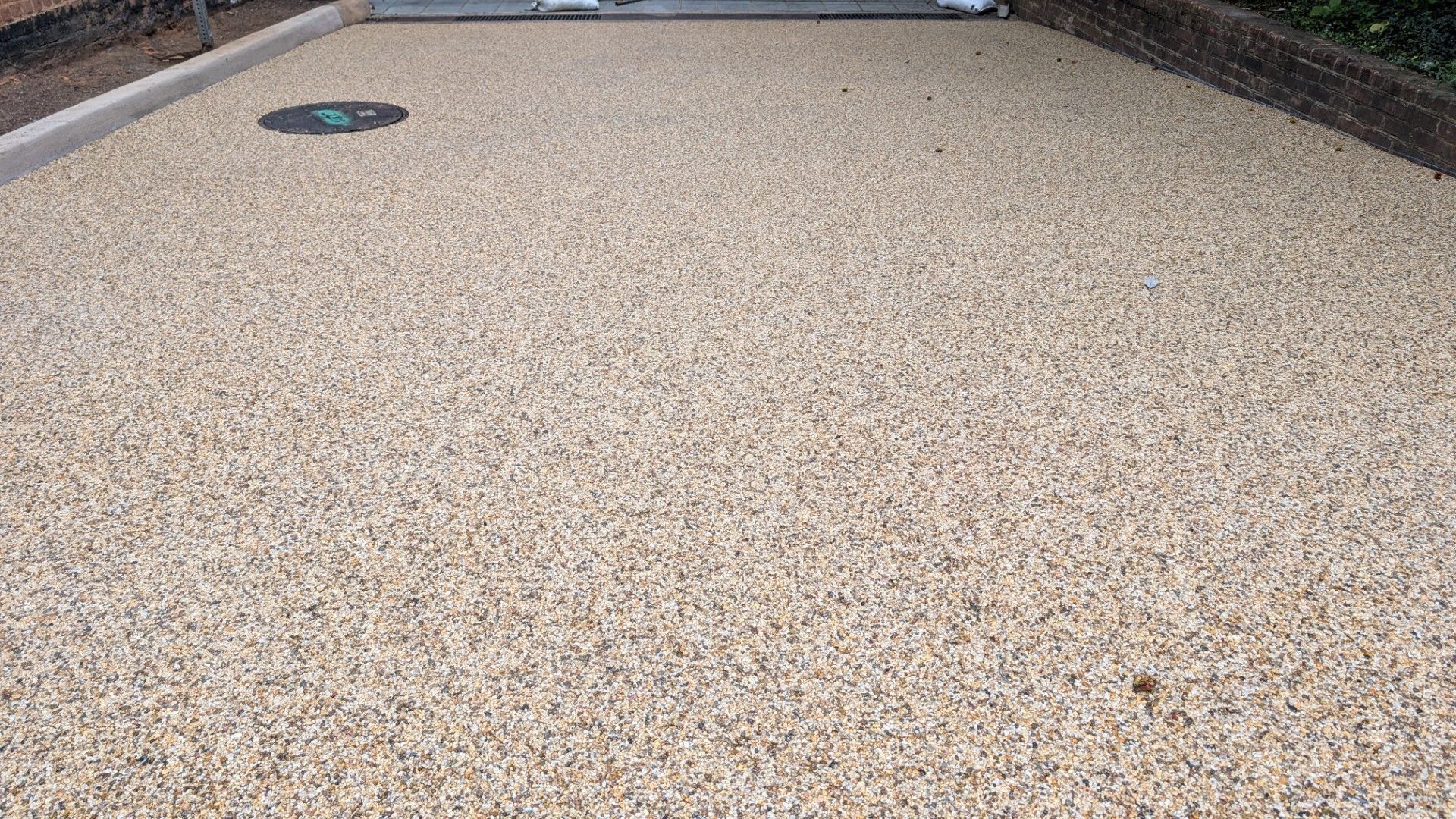 Empty beige gravel driveway with a small round drain cover near the top left.