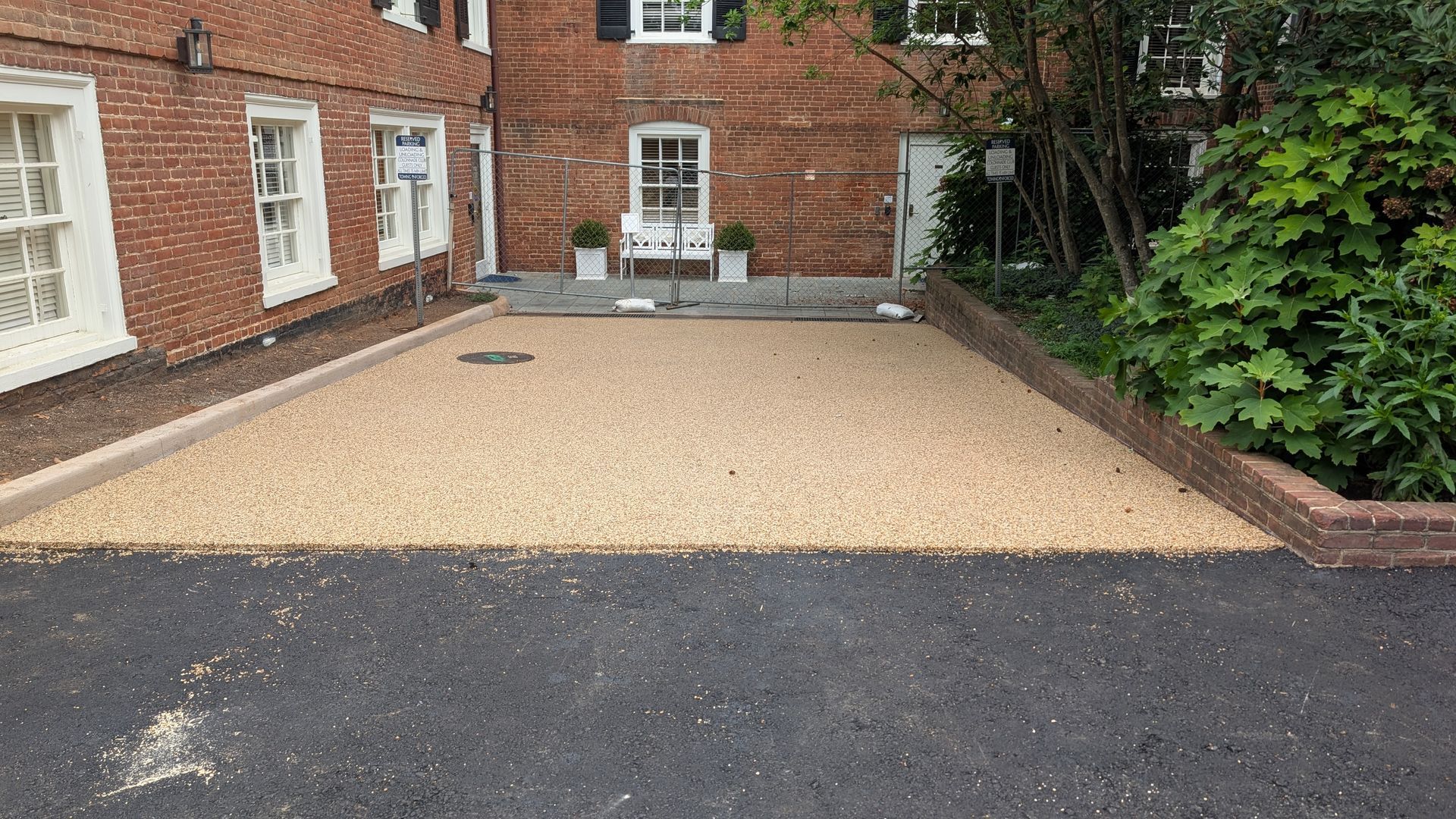 Gravel driveway beside a red brick house, bordered by low brick edging and greenery.