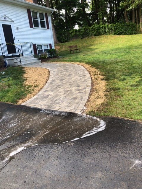 Brick walkway leading from asphalt driveway to white house with red shutters; green lawn.