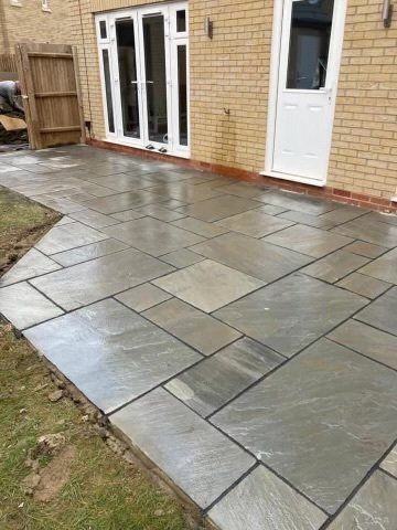 Newly laid grey flagstone patio next to a light brick house and a grassy area.