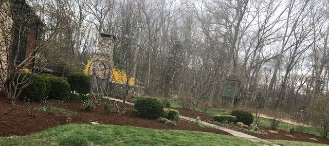 Stone chimney, garden path and shrubs, trees in the background. Overcast sky.