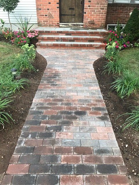 Brick walkway leading to a home's brick steps and front door, with flower beds on either side.