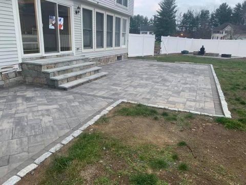 Backyard patio with steps and pavers. Light gray stones, border, grass.