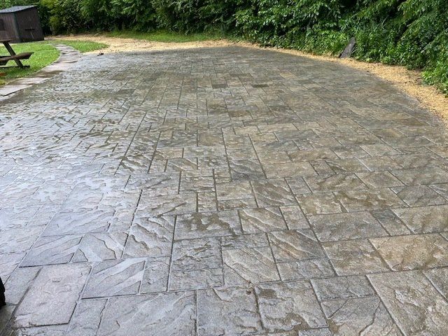 Wet, patterned concrete patio with gravel border; green foliage in background.