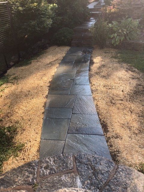 Stone walkway winding through a garden, bordered by straw-colored mulch.