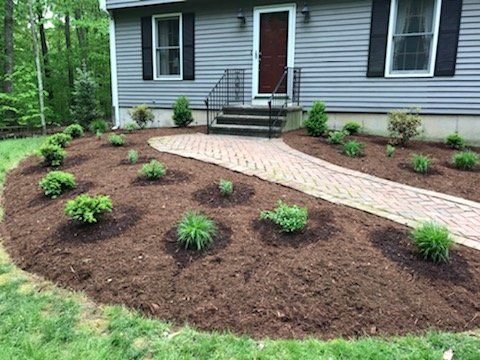 Gray house with brick walkway and landscaped flower beds covered in mulch.