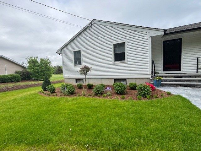 White house with landscaped garden bed, green lawn, and a cloudy sky.