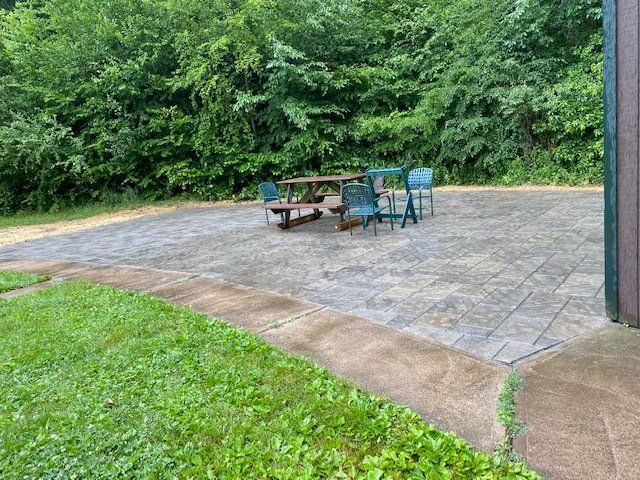 Outdoor patio with a table and chairs, surrounded by grass and trees.