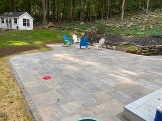 Backyard patio with chairs, a shed, and grassy area with trees in the background.