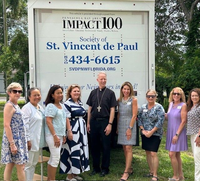 A group of people standing in front of an impact 100 sign