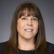 Portrait of a smiling person with straight brown hair against a gray background
