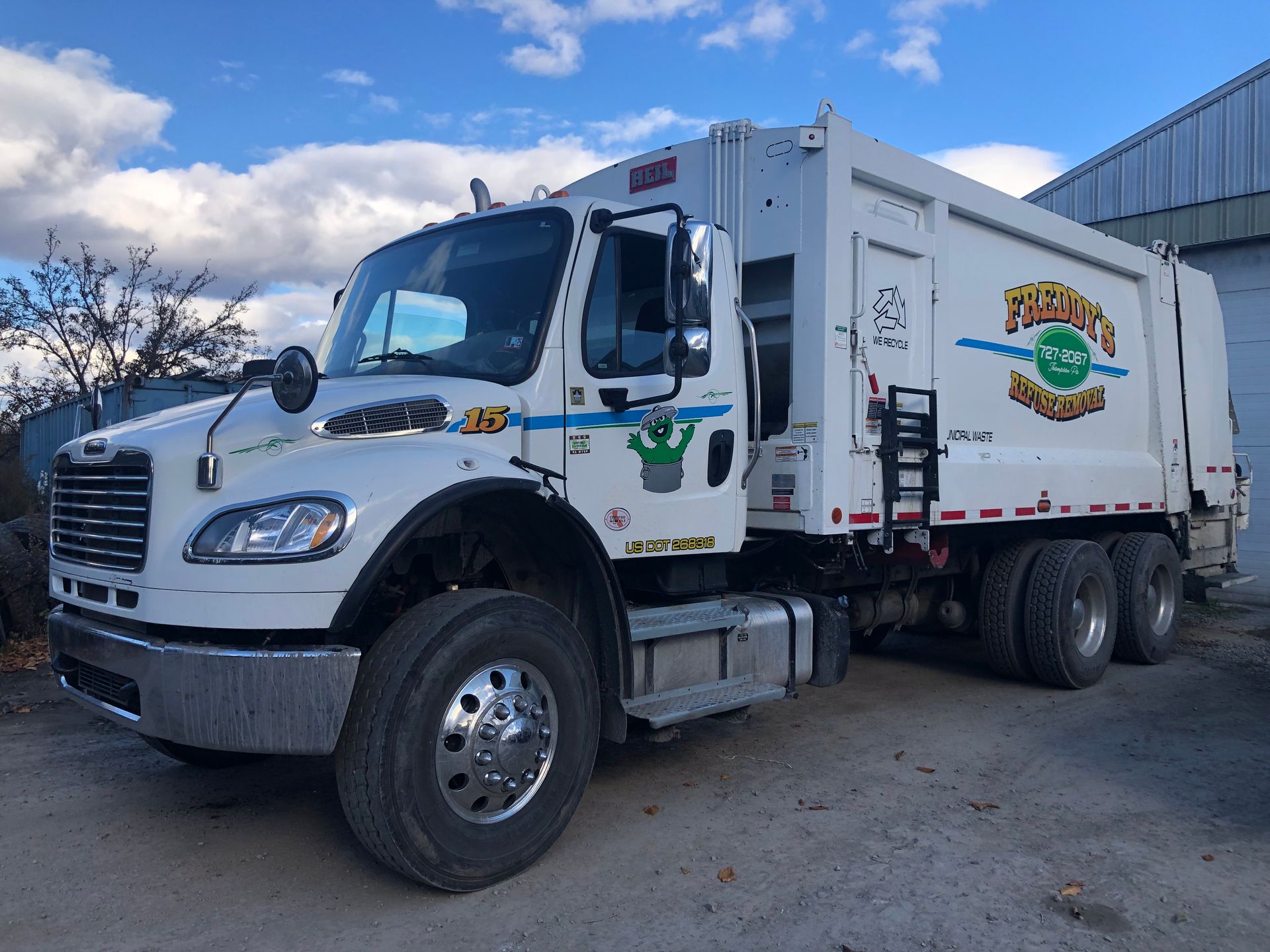 A white garbage truck is parked in front of a building