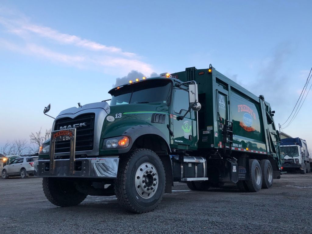 A green garbage truck is parked in a parking lot