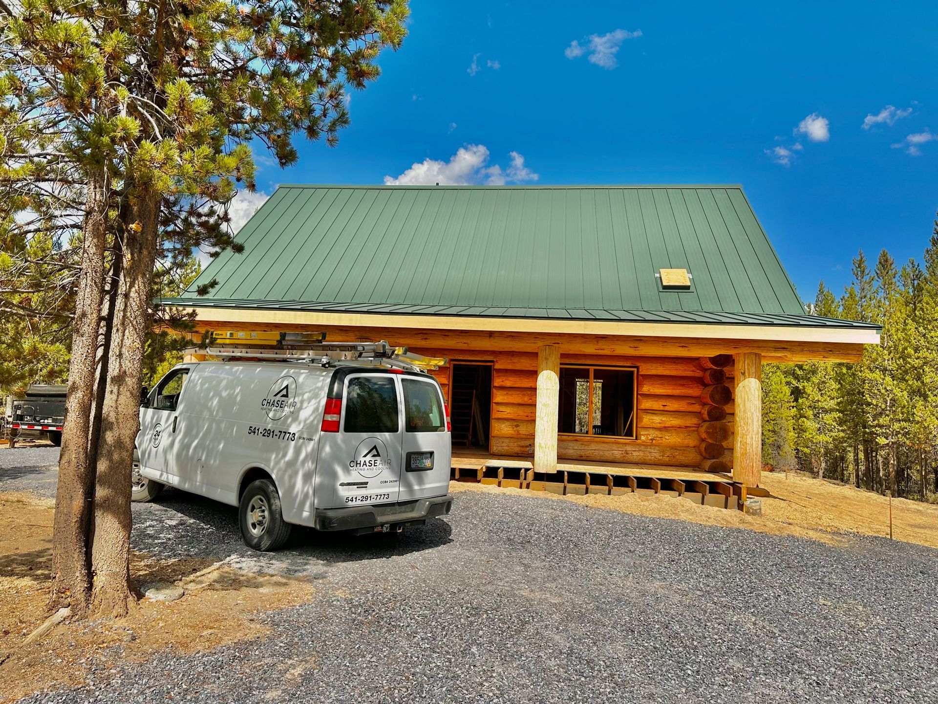 A white van is parked in front of a log cabin with a green roof.