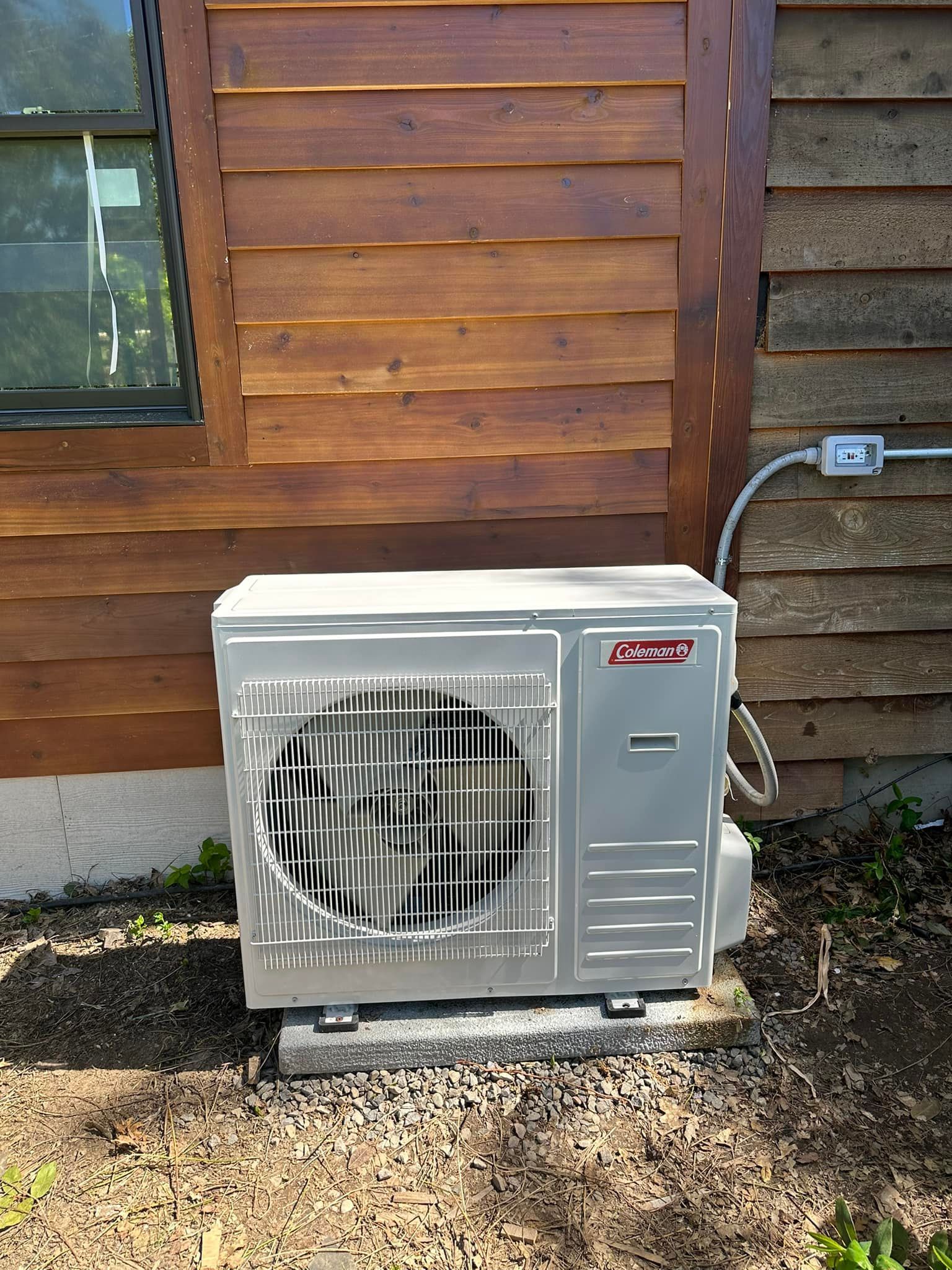 A white air conditioner is sitting outside of a wooden house.