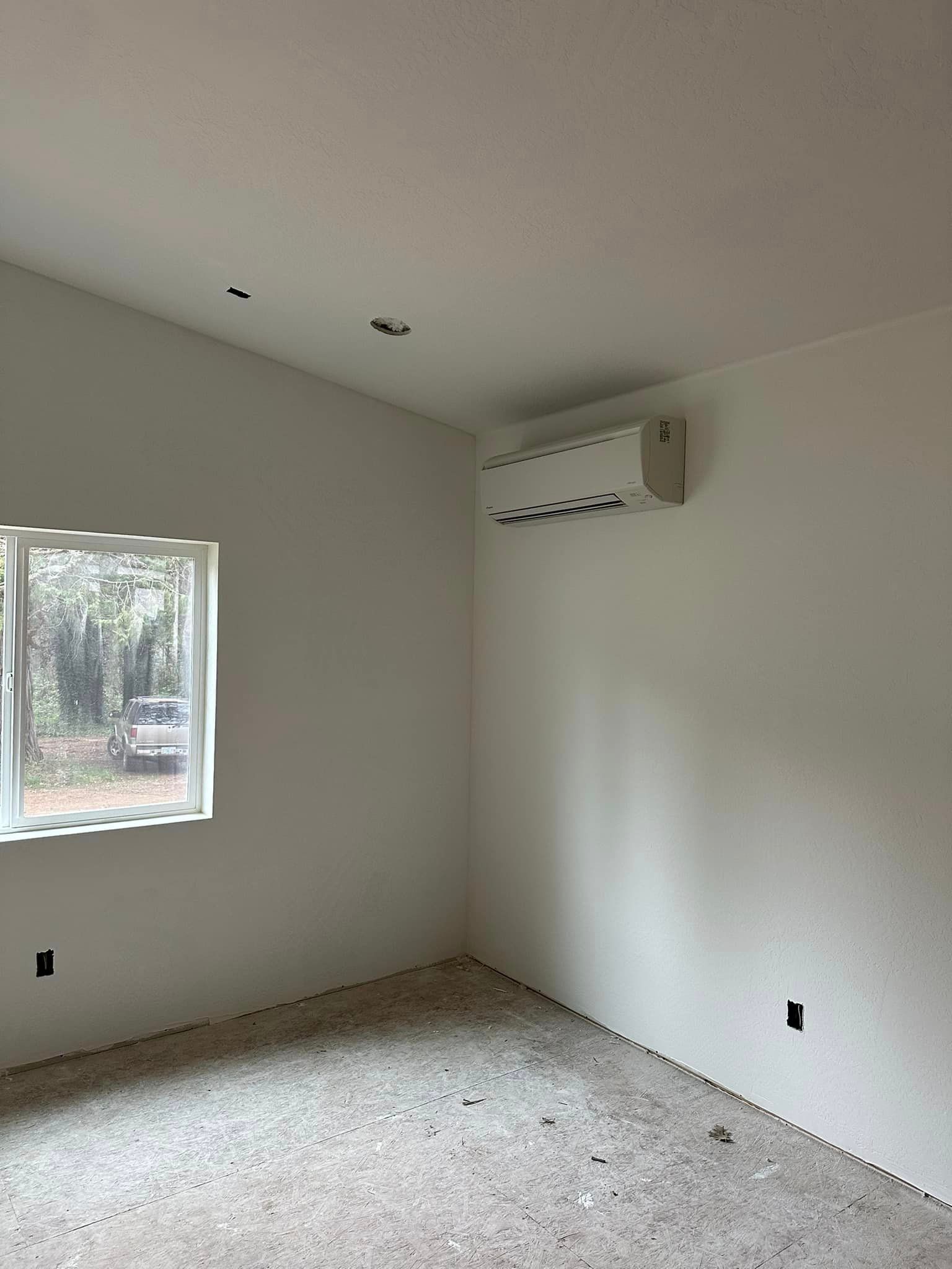 An empty room with a window and air conditioner on the wall.