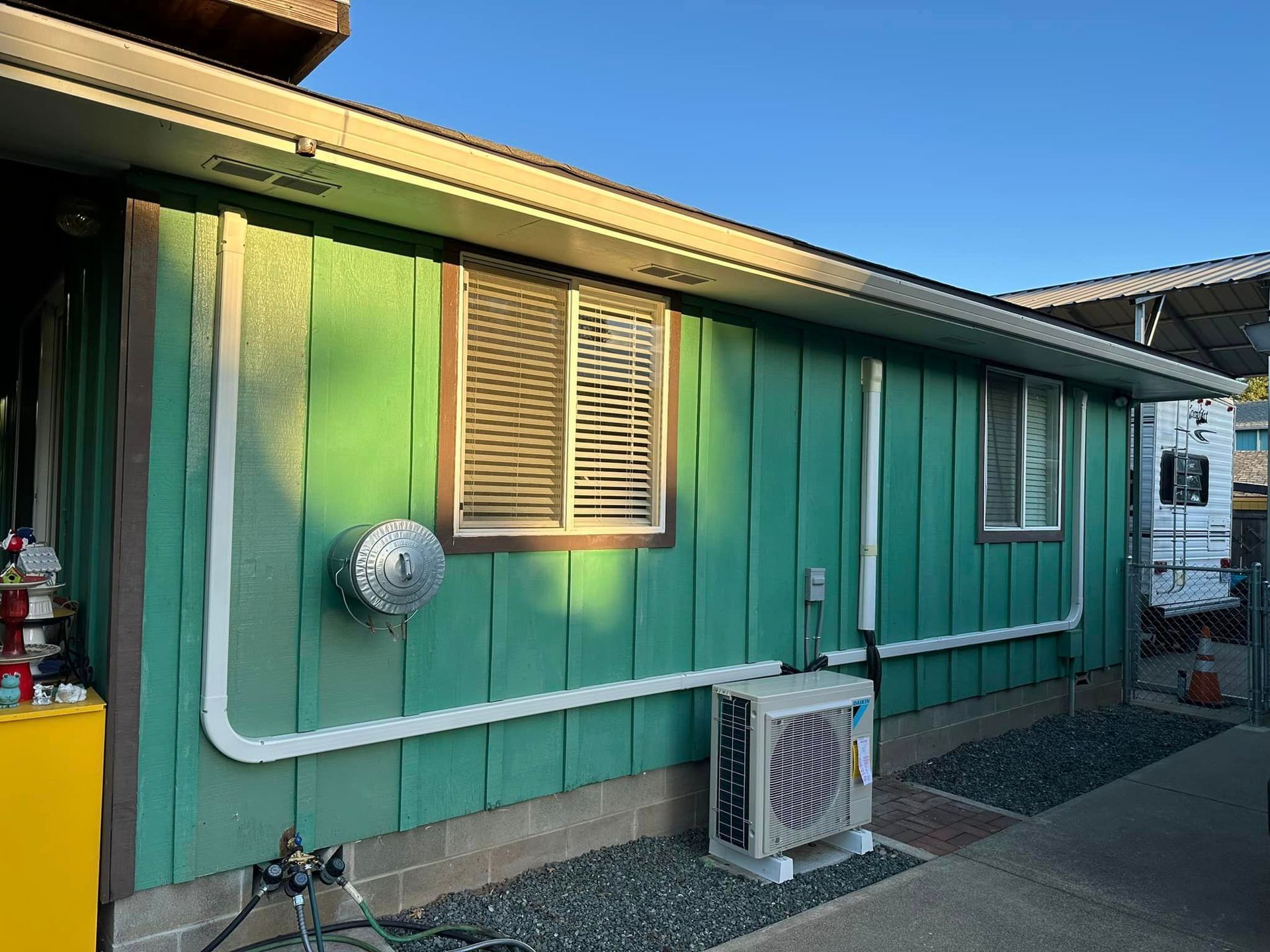 A green house with a window and an air conditioner on the side.