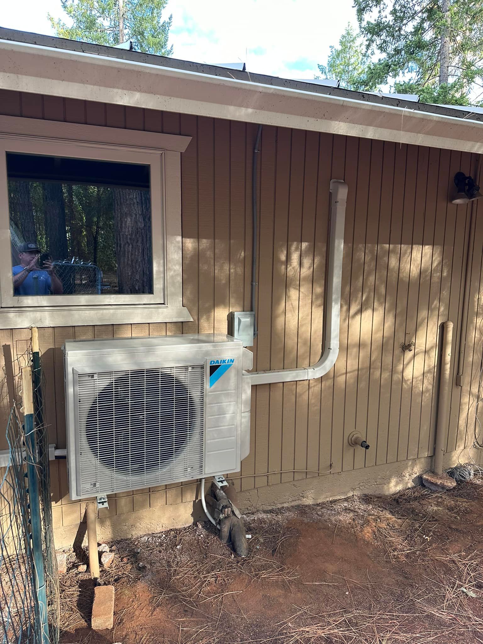 An air conditioner is installed on the side of a house next to a window.