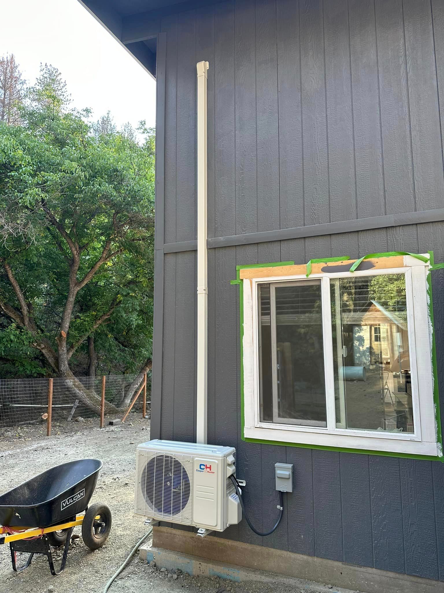 A wheelbarrow is parked in front of a house with a window and a fan.
