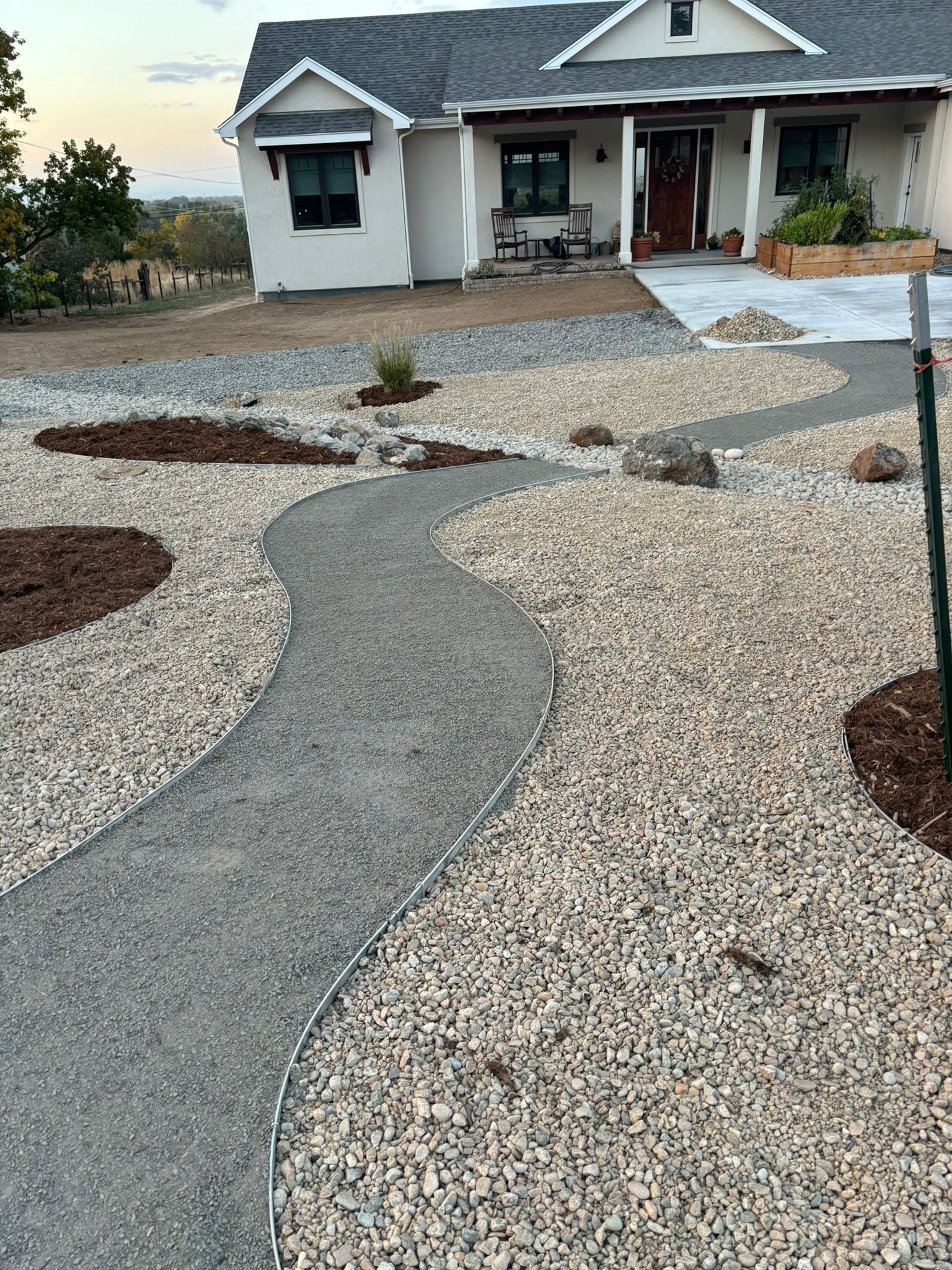 Curved gravel pathway leading to a white house with a porch and desert landscaping at dusk