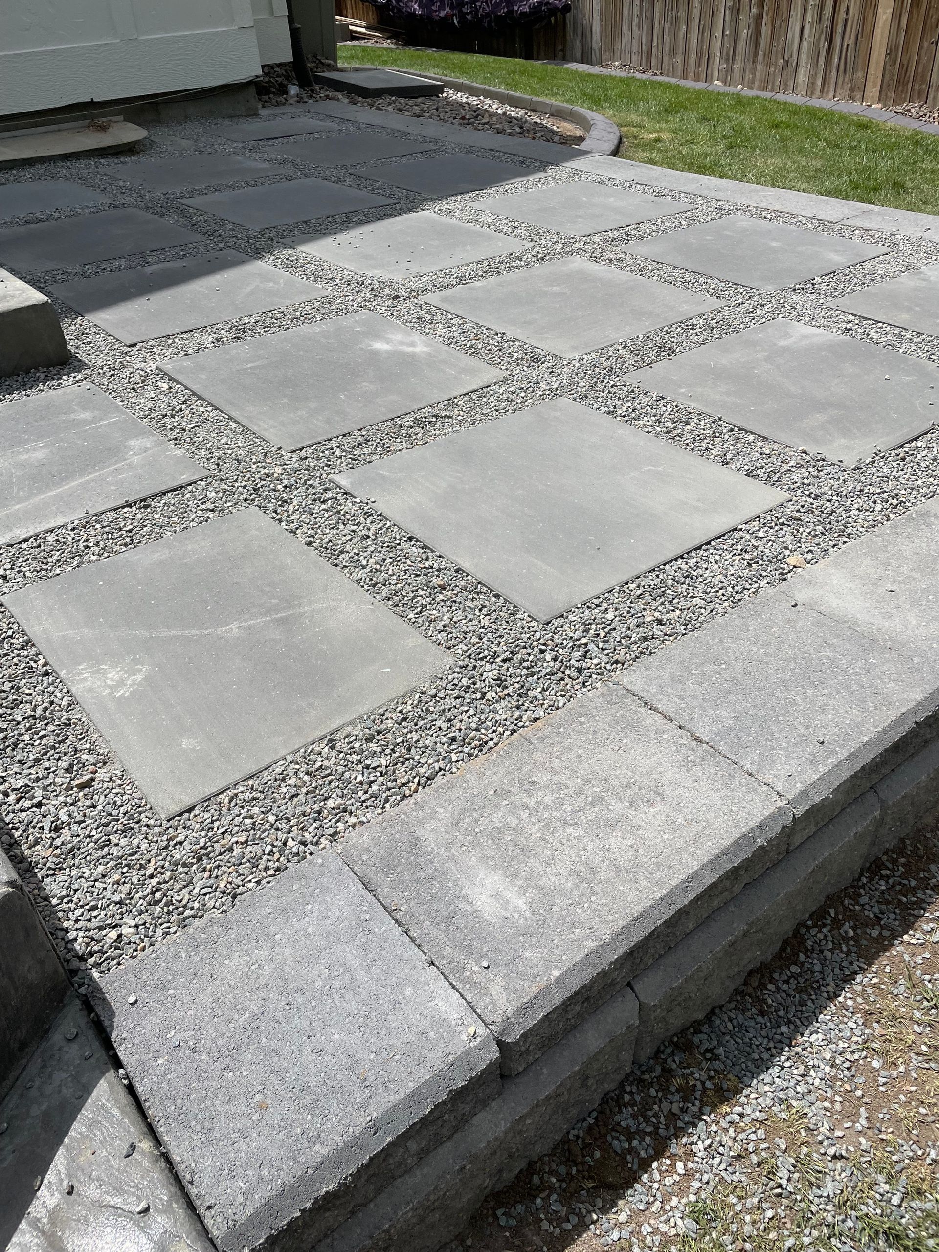Gray concrete stepping-stone patio bordered by dark gravel and a black deck surface.