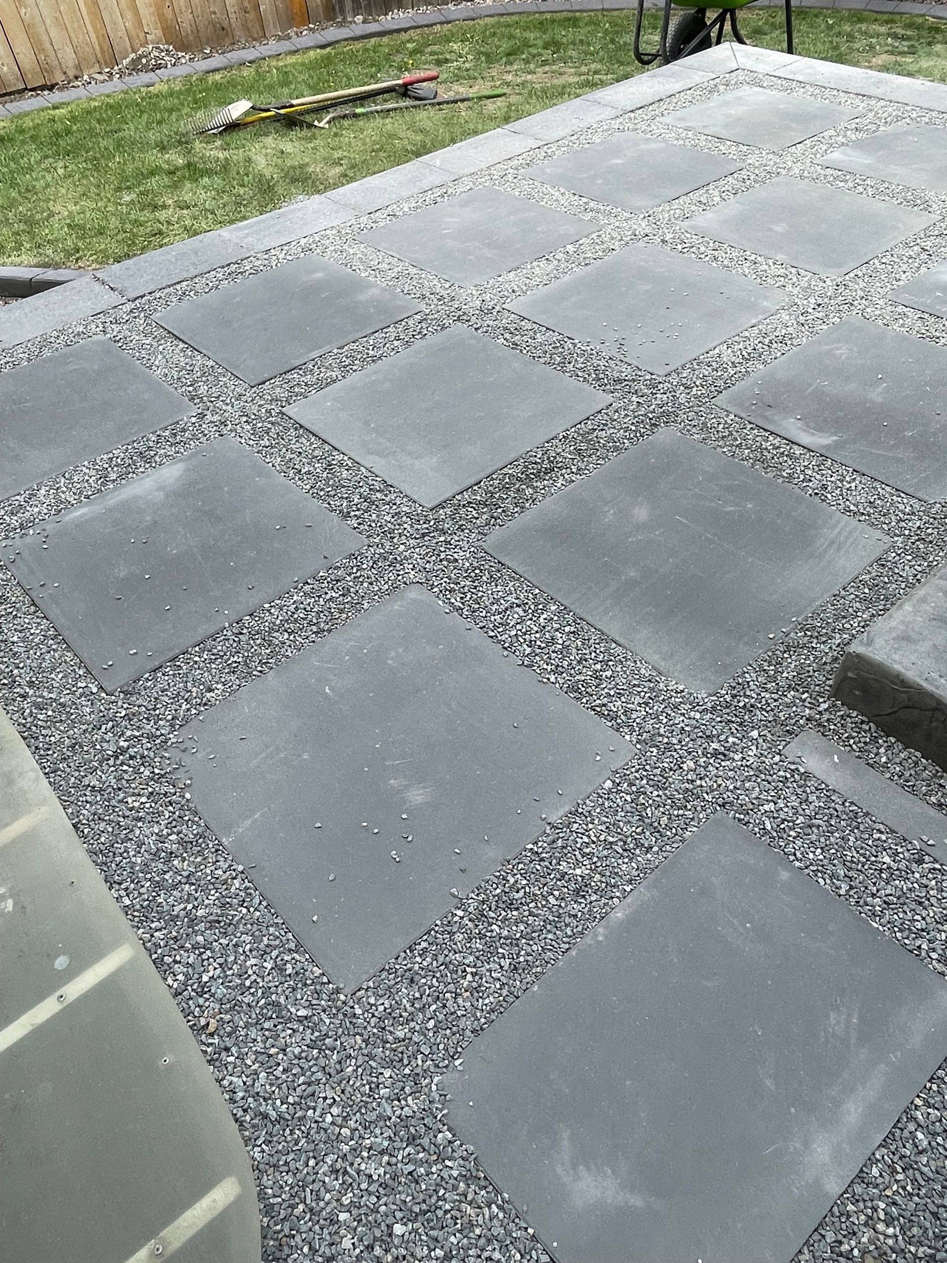 Gray stone pavers set in gravel, forming a modern patio or walkway beside a grassy lawn.