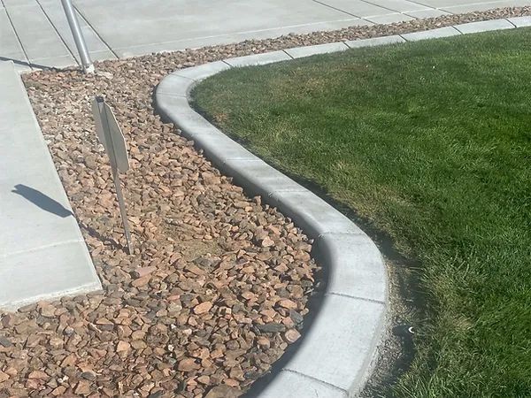 Curved concrete curb edging a rock bed beside a sidewalk and green lawn