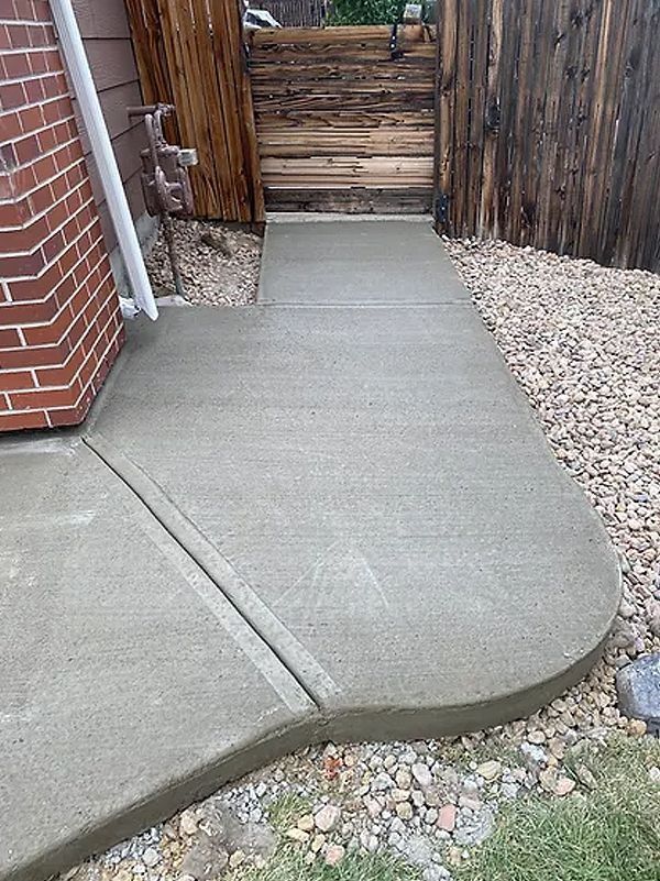 Concrete sidewalk and curved ramp beside a brick wall, gravel border, and wooden fence.
