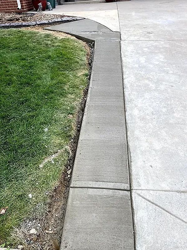 Curved concrete sidewalk beside a grassy lawn and driveway edge