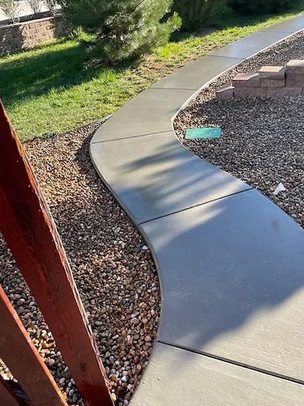 Curved concrete walkway beside gravel landscaping and grass in a sunny yard