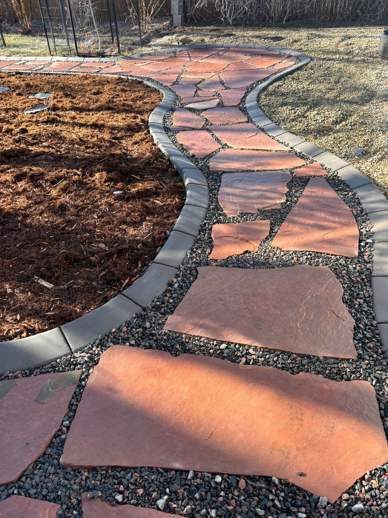 Curving flagstone garden path with gray edging beside mulch and gravel