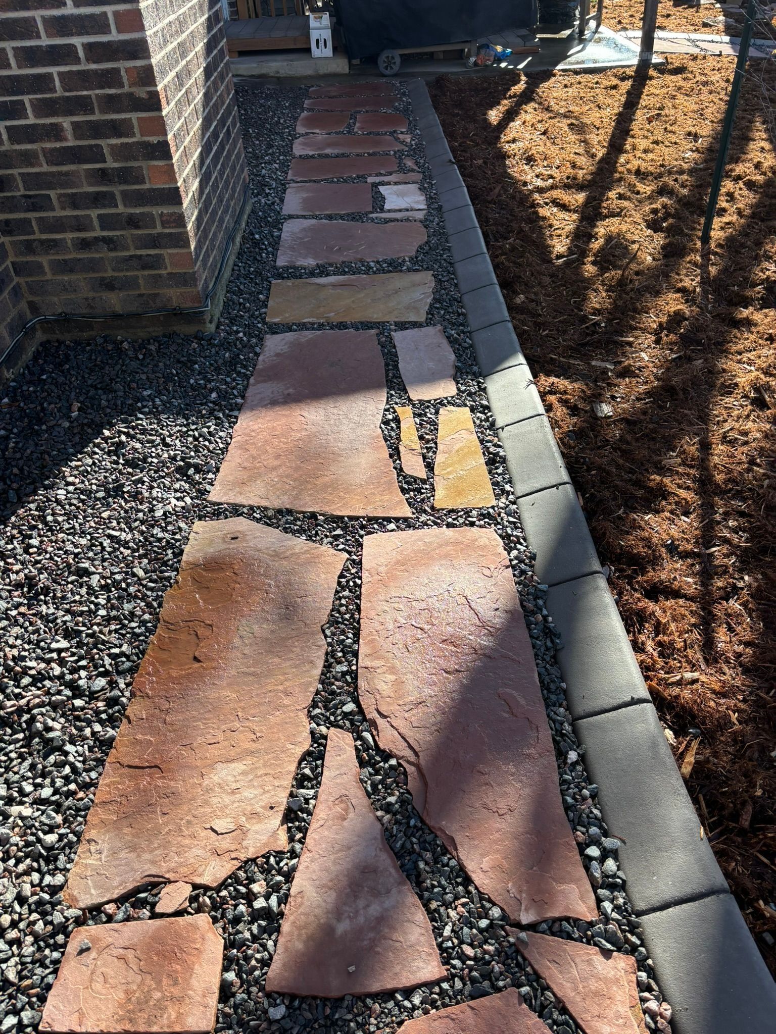Stone walkway with broken reddish pavers beside a house and gravel border