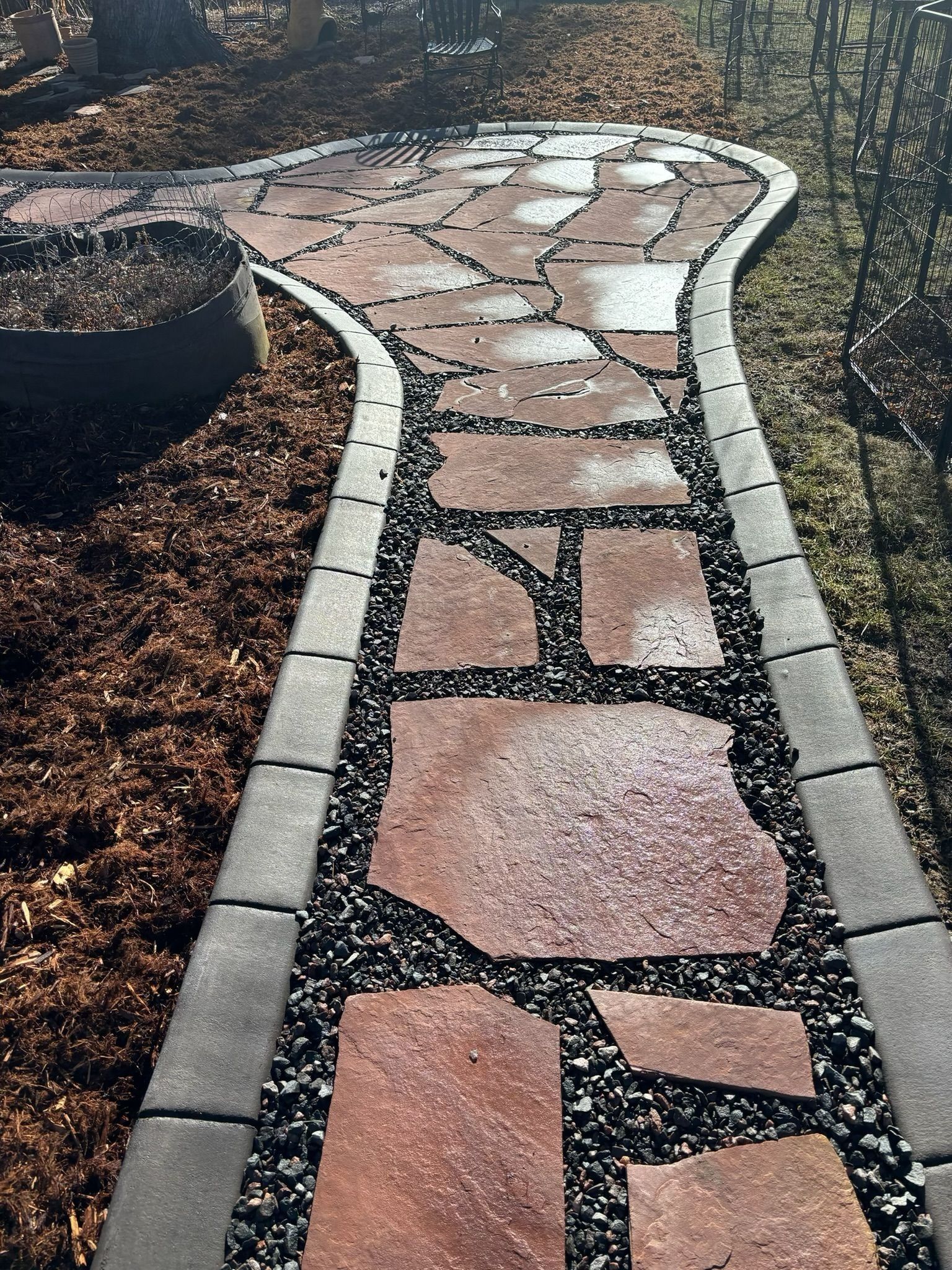 Curving stone garden path with pink paving stones and gray border blocks in a dry landscape