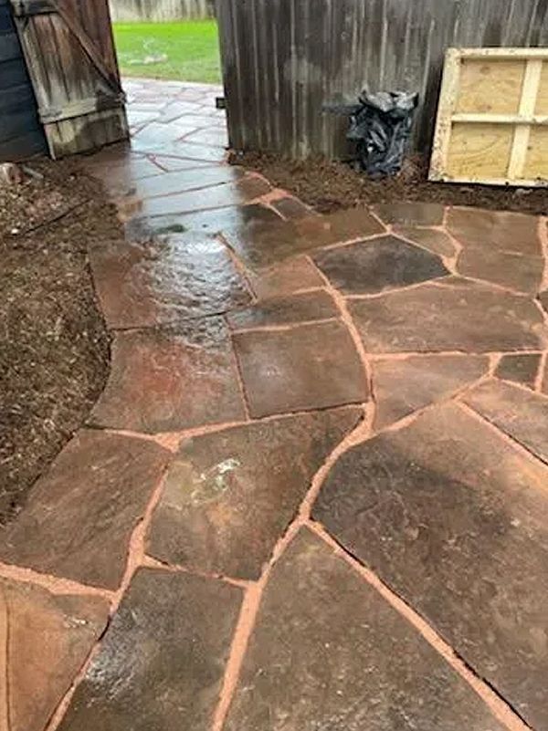 Wet stone patio with irregular flagstones beside a wooden fence and shed.