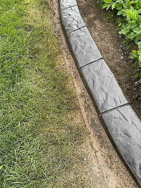 Curved gray stone garden edging beside a grassy lawn and soil bed
