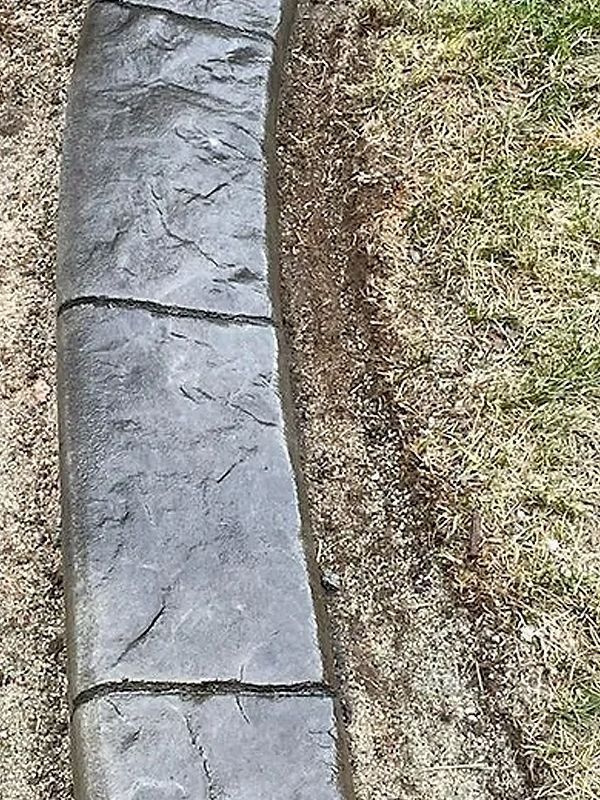 Curved stone edging beside a grassy lawn and dirt strip