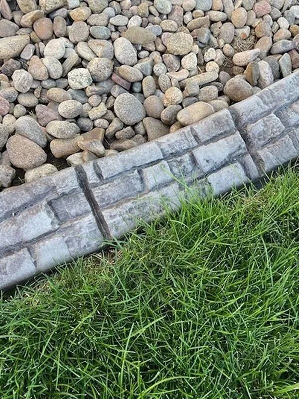 Stone border between decorative pebbles and green grass in a landscaped yard